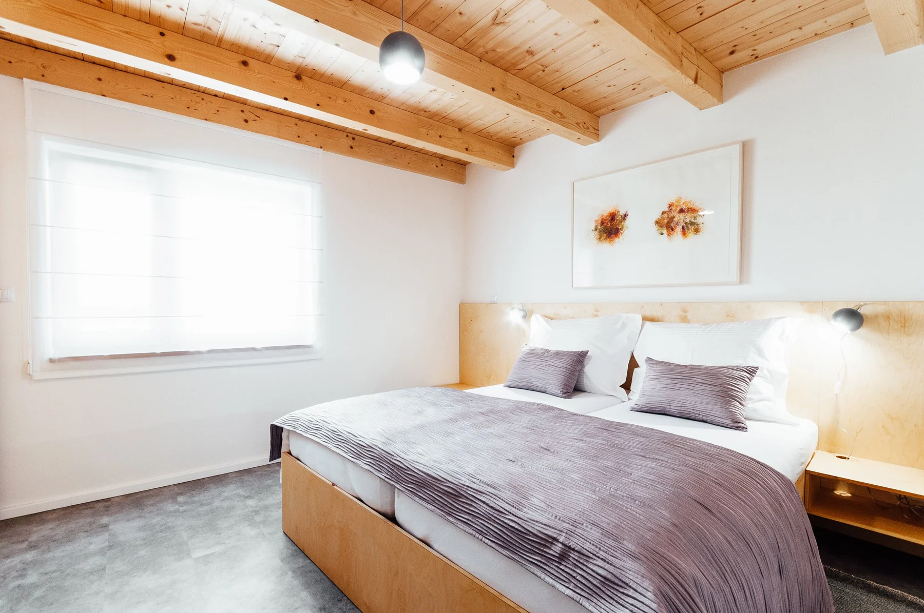 Světlá ložnice rodinného apartmánu s dvojlůžkem a dřevěnými trámy